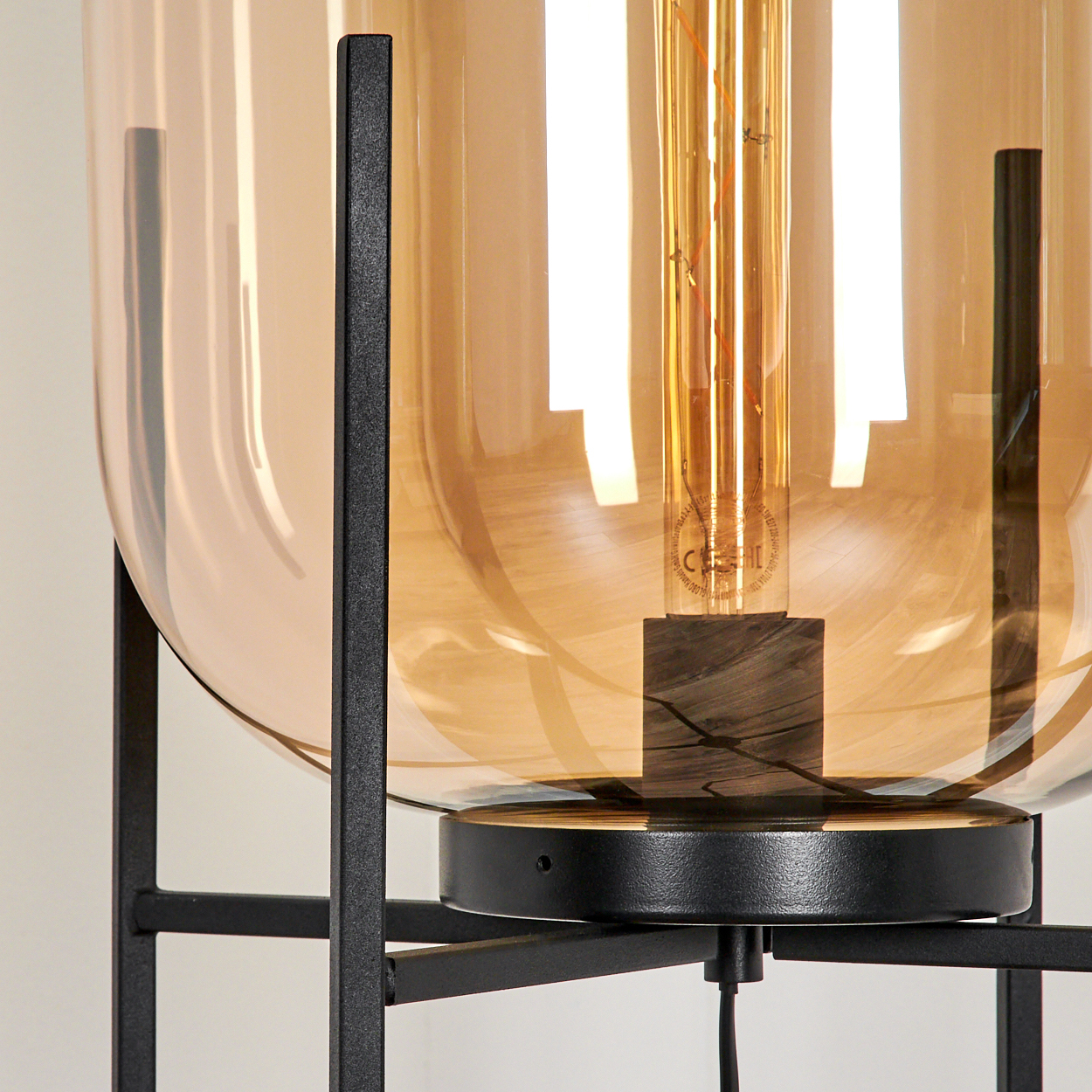 Nahaufnahme einer modernen Lampe. Sie hat einen großen bernsteinfarbenen Glasschirm, eine sichtbare Glühbirne und ein schwarzes Metallgestell.