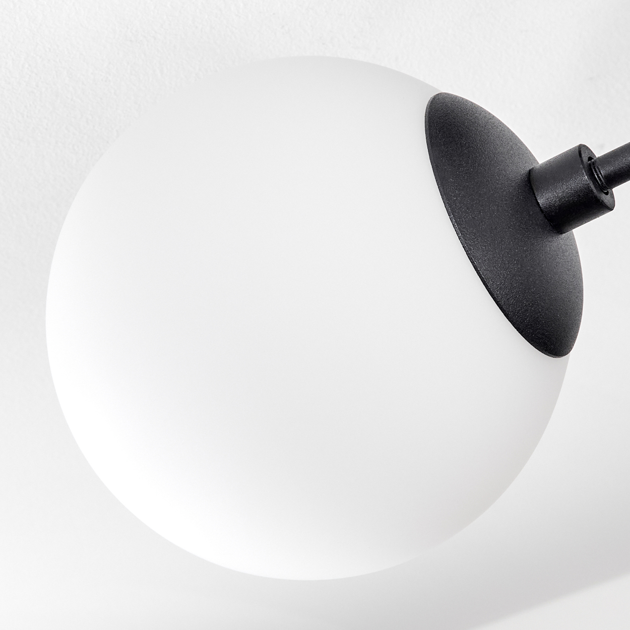 Eine weiße, kugelförmige Leuchte mit schwarzem Sockel und Arm ist an einer weißen Wand befestigt. Nahaufnahme der Leuchte.