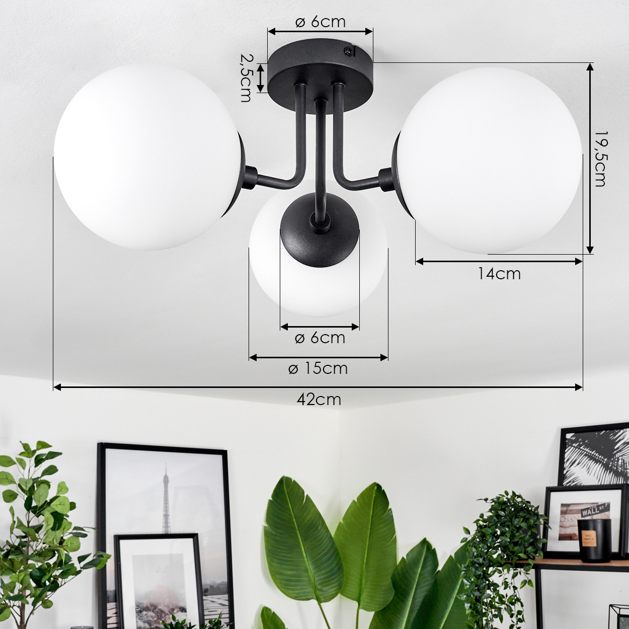 Eine schwarze Deckenlampe mit drei weißen Kugeln wird angezeigt. Abmessungen sind angegeben. Im Hintergrund Pflanzen und gerahmte Bilder.