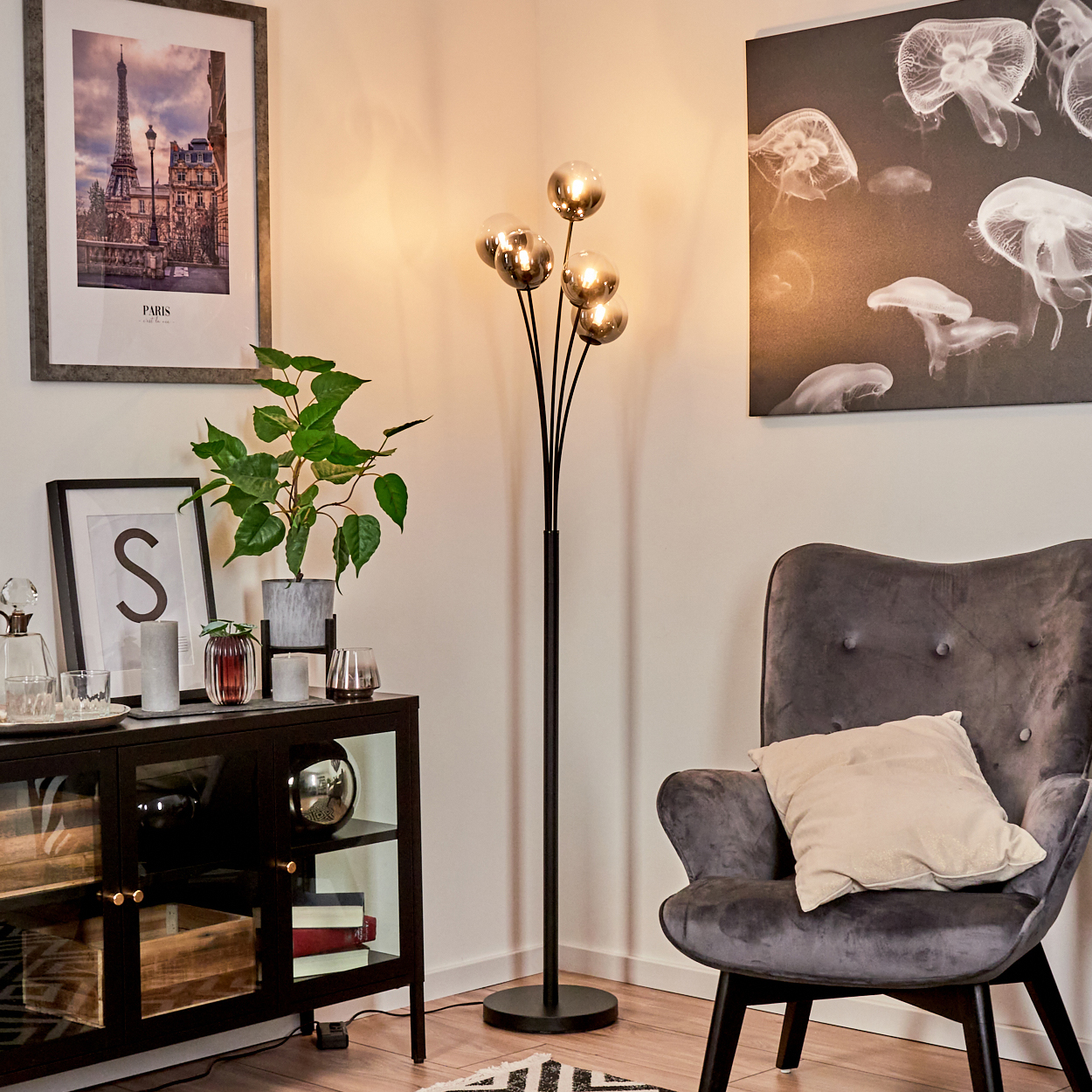 Ein Zimmer mit Stehlampe, Schrank, grauem Sessel und einem Gemälde von Quallen. Ein Pariser Bilderrahmen ist an der Wand.