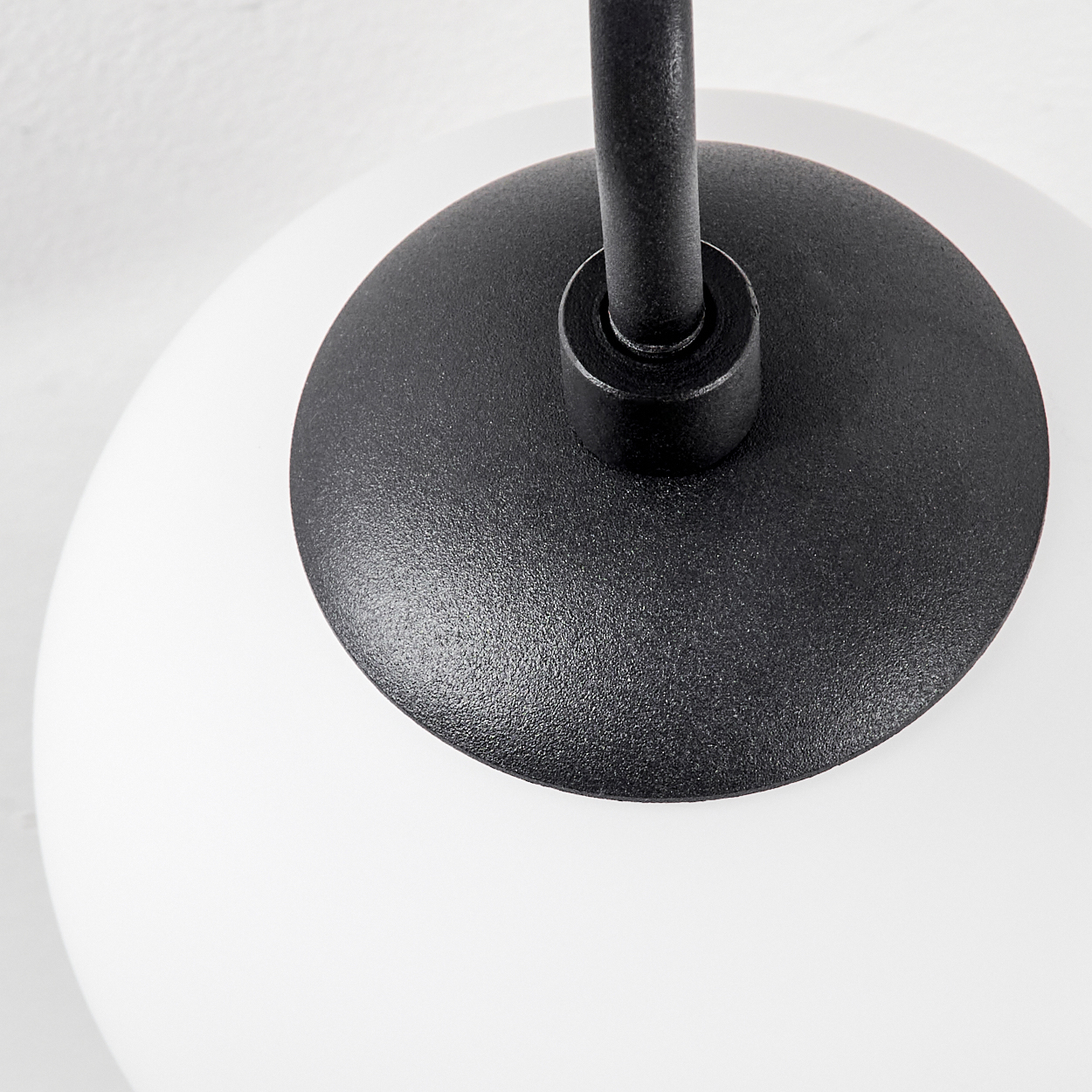 Nahaufnahme einer modernen Lampe. Ein schwarzer Metallsockel trägt einen weißen, runden Glasschirm. Eine schwarze Metallstange ragt nach oben.