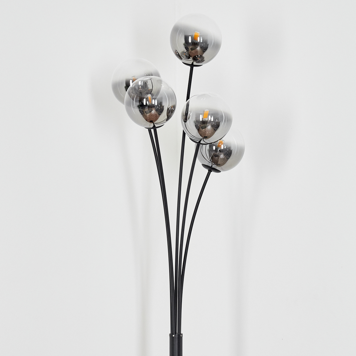 Eine moderne Stehlampe mit sechs kugelförmigen, verspiegelten Glasschirmen auf schwarzen Stielen. Der Hintergrund ist eine weiße Wand.