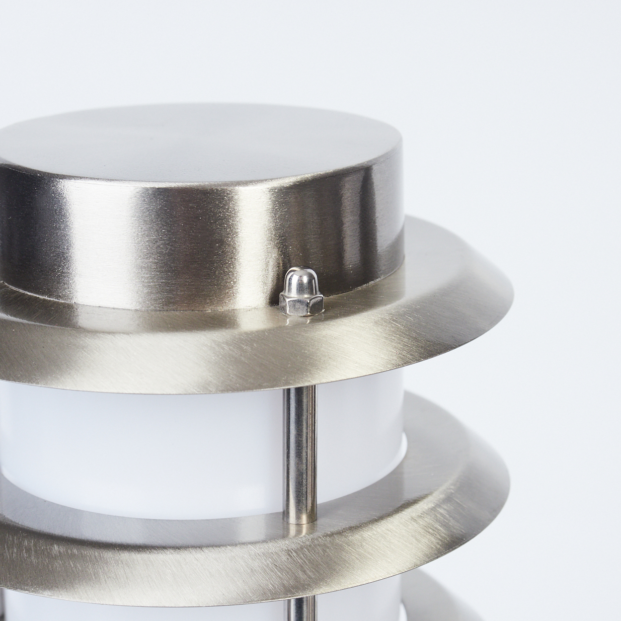 Nahaufnahme einer Lampe. Sie hat eine silbermetallic Oberfläche mit zylindrischem Oberteil und weißem Lichtdiffusor. Eine kleine Mutter sichert die Oberseite.
