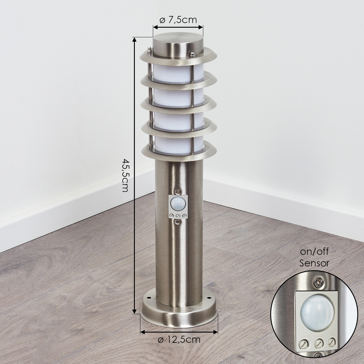 Edelstahl-Außenleuchte mit Sensor. Sie steht auf Holzboden, in der Nähe einer weißen Wand.