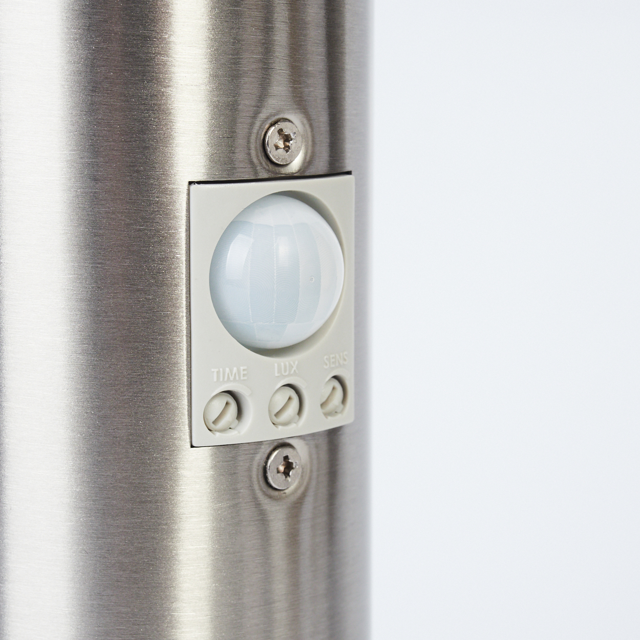 Ein Metallzylinder mit Sensor. Der Sensor hat eine weiße Kuppel und Knöpfe mit der Aufschrift 'TIME', 'LUX' und 'SENS'. Schrauben befestigen die Teile.