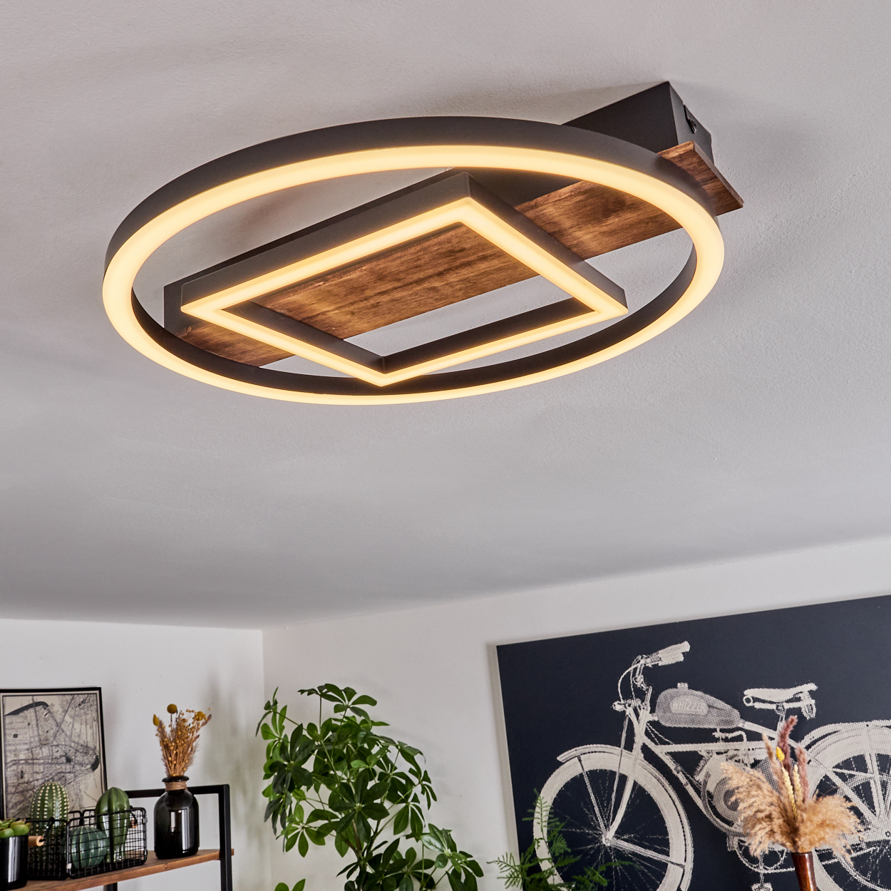 Moderne Deckenleuchte mit Holz- und Metalldesign, das warmes Licht ausstrahlt. Der Raum hat Pflanzen und ein Fahrradkunstwerk an der Wand.