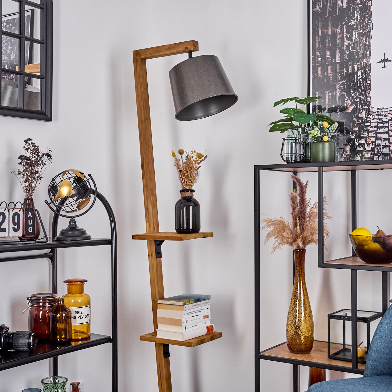 Innenraum mit Holzlampe, Regalen mit Deko, Büchern, Vasen mit Blumen und Globus. Ein schwarz gerahmter Spiegel ist sichtbar.