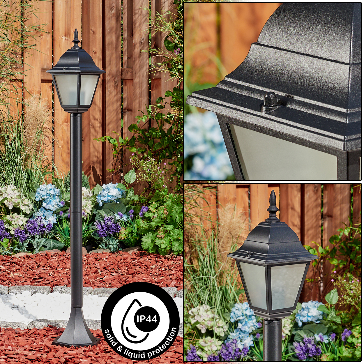 Eine schwarze Außenlaterne mit dekorativer Spitze. Die Lampe befindet sich in einem Garten mit Blumen, Mulch und einem Holzzaun.