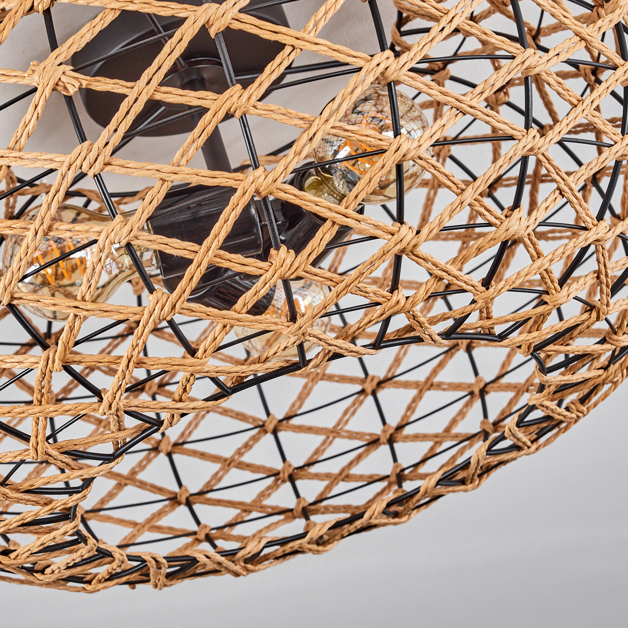 Nahaufnahme einer gewebten Lampe. Kordel aus Korbgeflecht und schwarzer Metallrahmen. Drei Glühbirnen sind sichtbar.