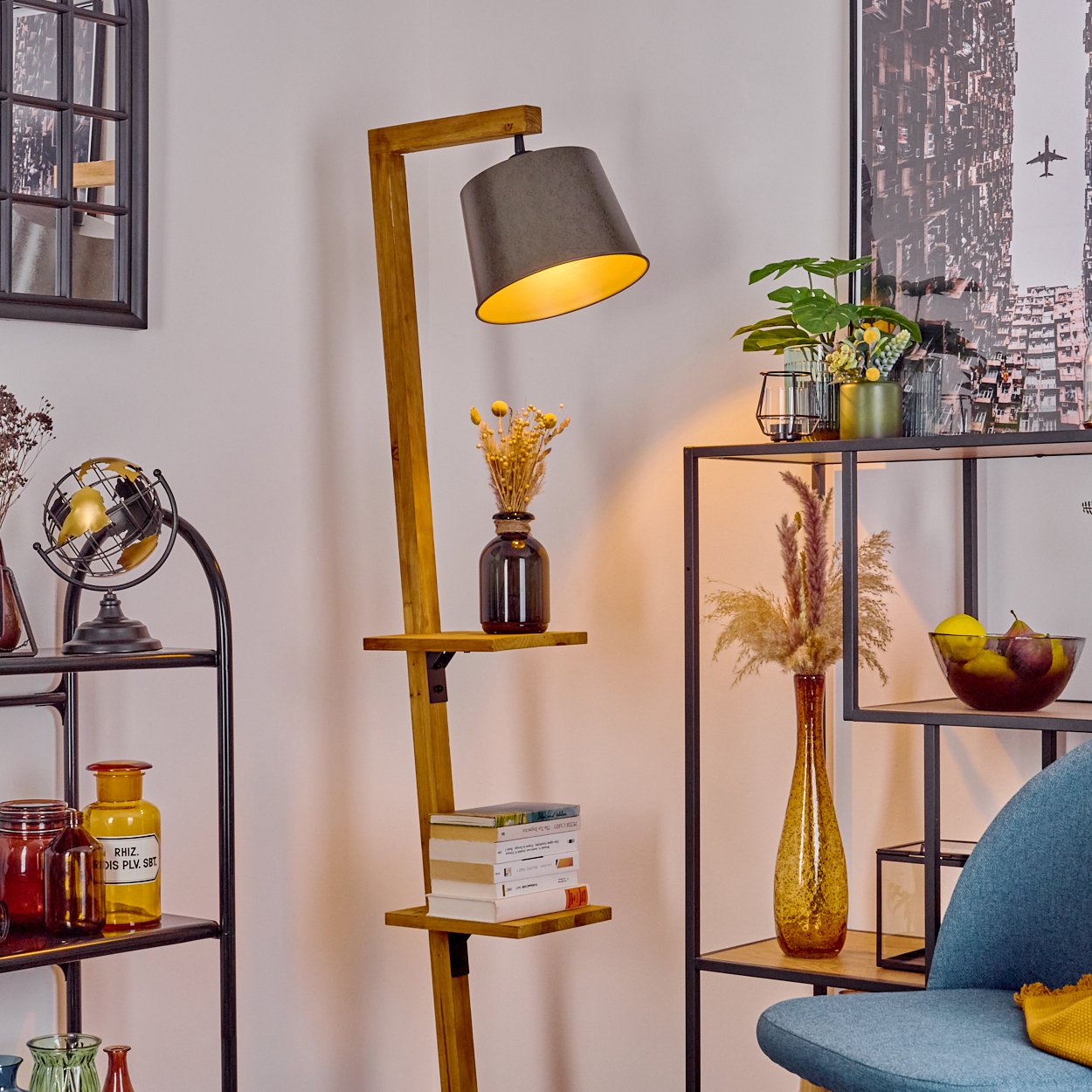 Innenraum mit Stehlampe, Regalen mit Deko, Stuhl und Poster einer Stadtlandschaft.