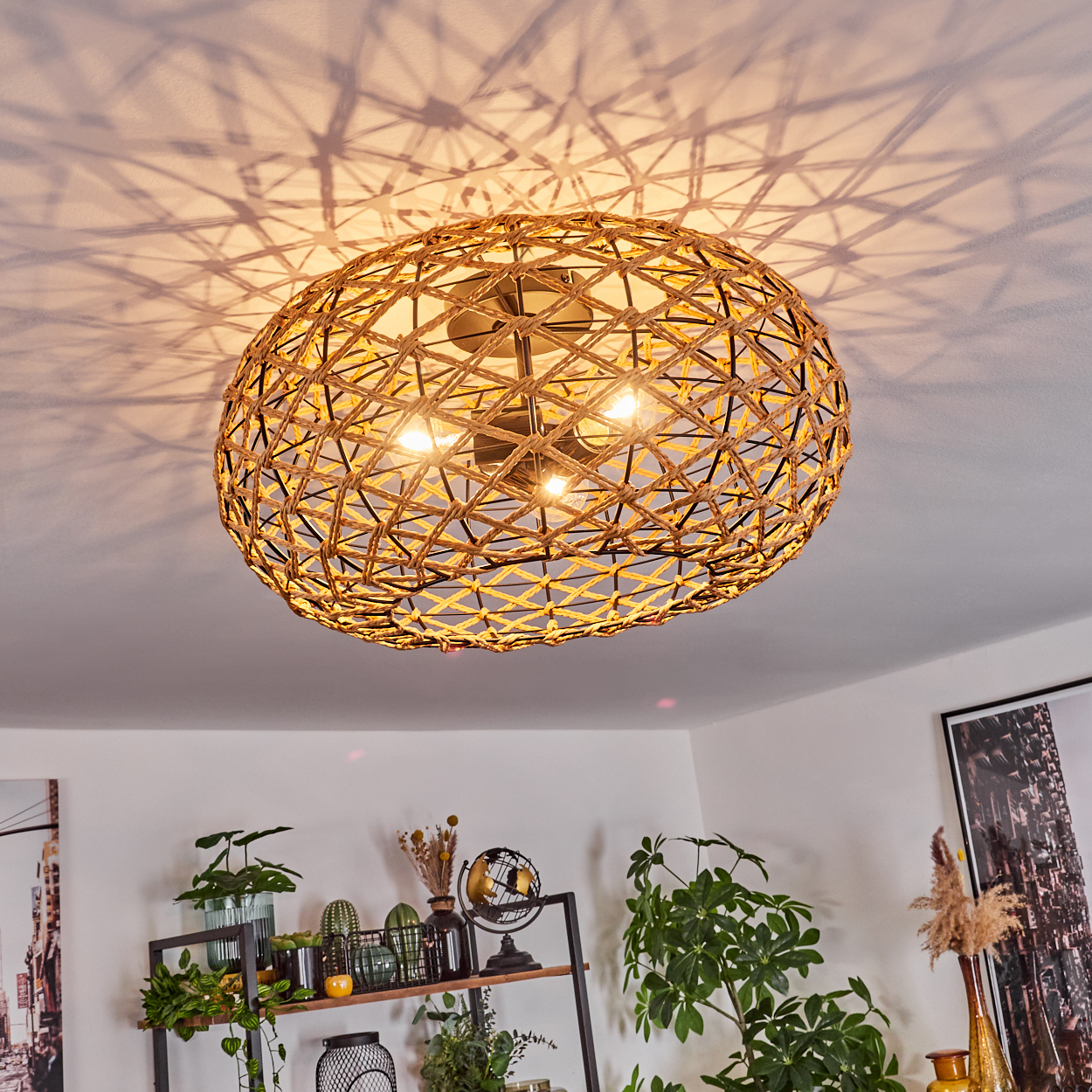 Eine gewebte Leuchte hängt von der Decke und wirft Schattenmuster. Darunter befindet sich ein Regal mit Pflanzen und Dekoration.