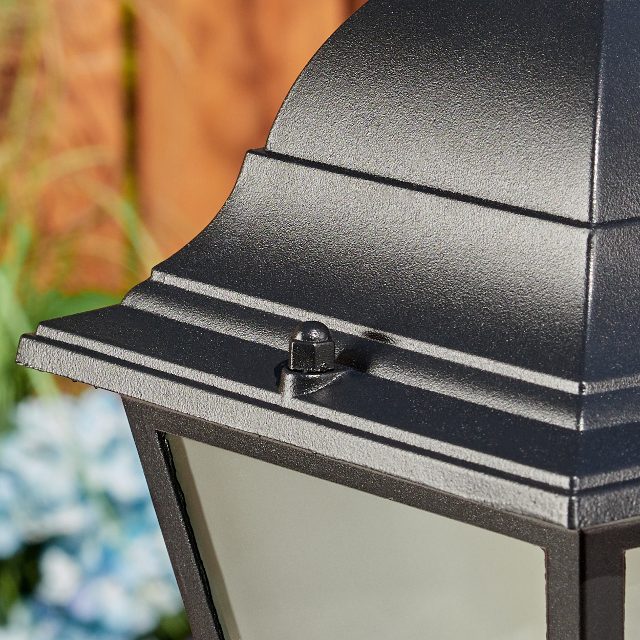 Nahaufnahme einer schwarzen Außenlampe. Details umfassen eine strukturierte Oberfläche, eine sichtbare Schraube und einen verschwommenen Hintergrund.