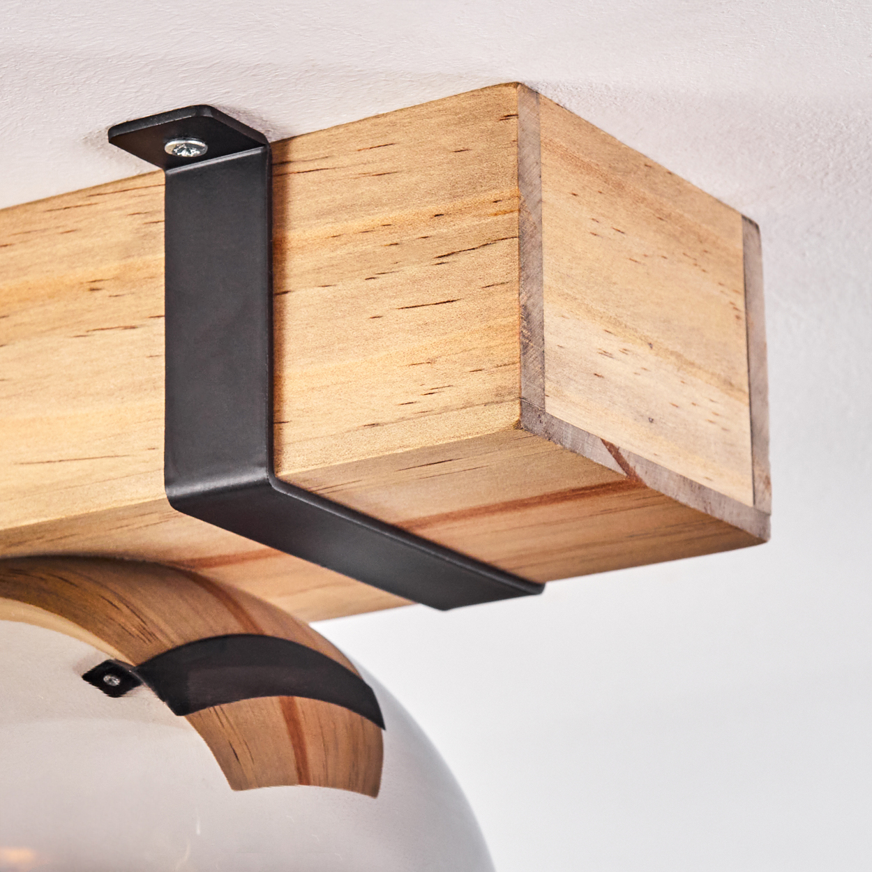 Holzbalken, gehalten von einer schwarzen Metallhalterung, an einer weißen Decke befestigt. Darunter ist eine kugelförmige Glaslampe zu sehen.