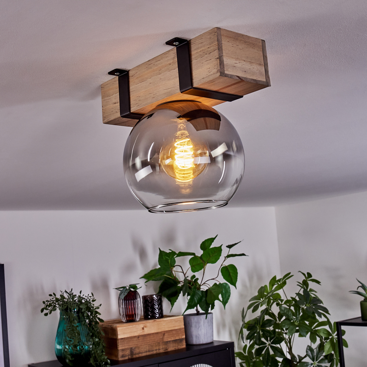 Deckenleuchte mit Holzbalken und Glaskugel. Pflanzen und eine Holzkiste befinden sich darunter.
