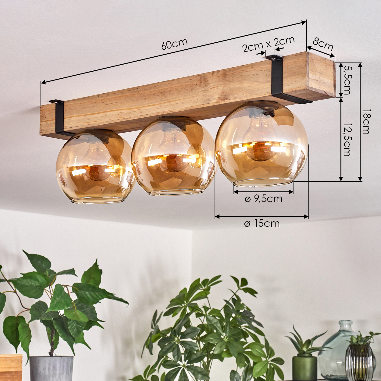 Deckenlampe mit drei bernsteinfarbenen Glaskugeln, die unter einem Holzbalken hängen. Maße sind angegeben. Grüne Pflanzen im Vordergrund.