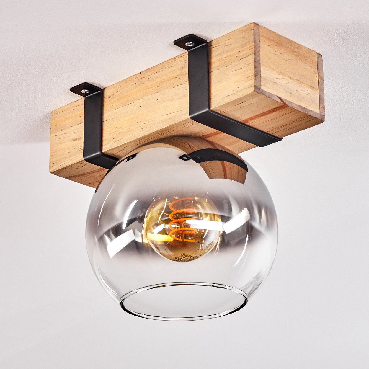 Eine Deckenleuchte aus Holzbalken mit Glasschirm. Sie hat eine warme Glühbirne darin.