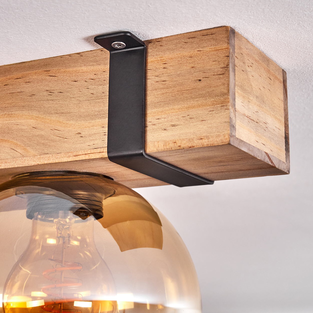 Nahaufnahme einer Holzbalken-Leuchte. Eine schwarze Metallhalterung stützt den Balken. Eine Glühbirne hängt darunter.