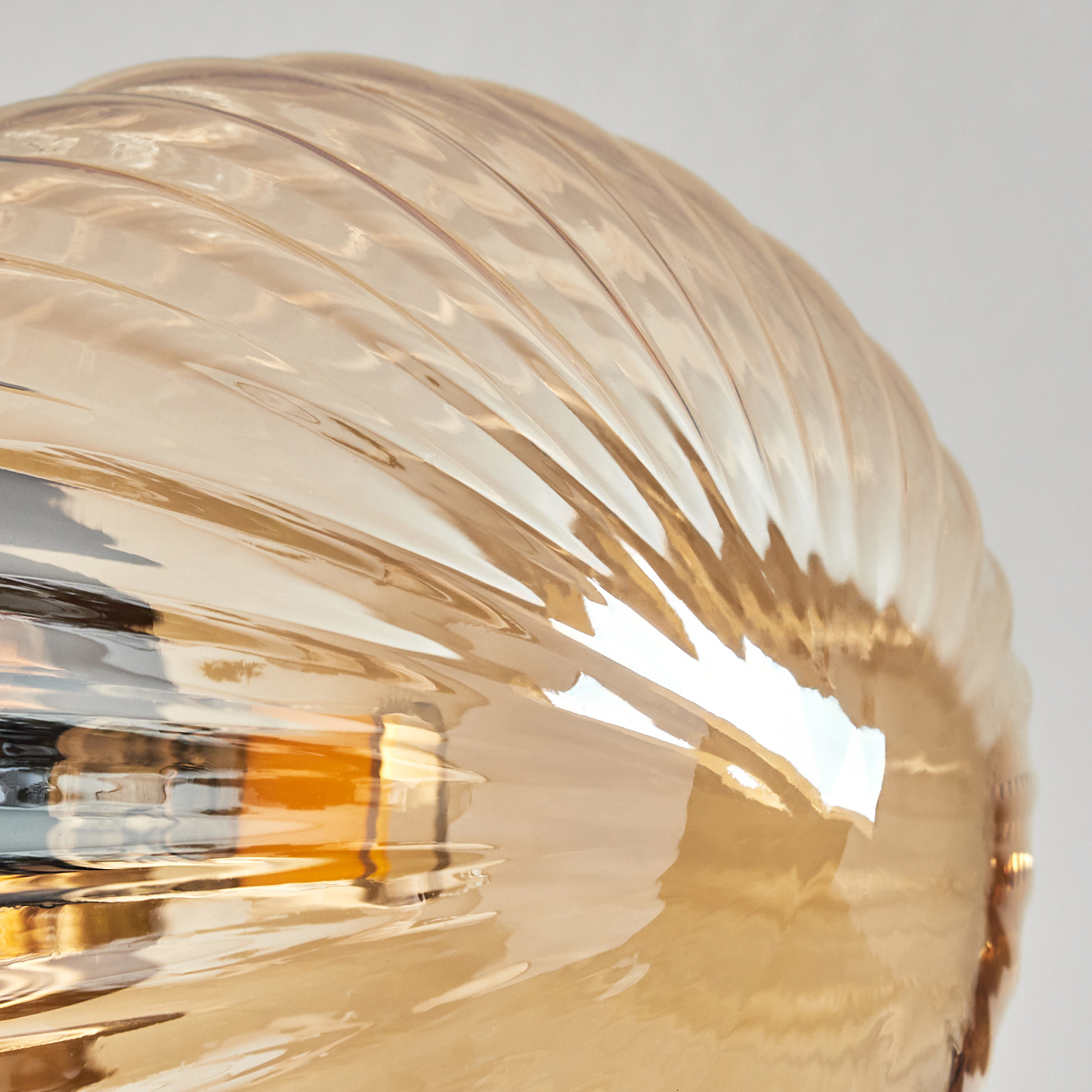 Nahaufnahme eines Glasschirms. Er ist bernsteinfarben, mit geriffelter Oberfläche, die Licht reflektiert. Der Hintergrund ist ein weicher, weißer Farbverlauf.