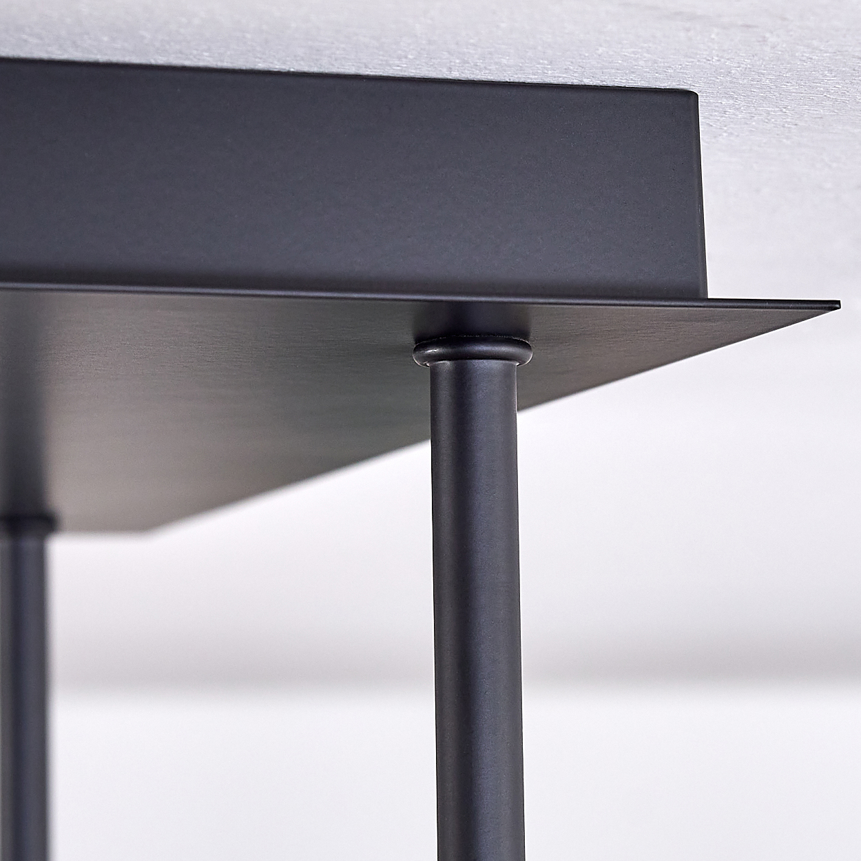 Nahaufnahme einer schwarzen, geometrischen Metallkonstruktion. Sie hat eine flache Oberfläche, die von zylindrischen Beinen getragen wird, vor weißem Hintergrund.