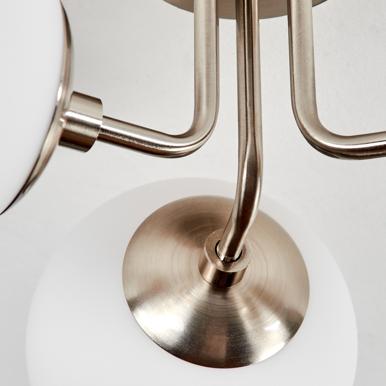 Nahaufnahme einer modernen Lampe. Sie hat einen Metallrahmen mit gebogenen Armen und weißen Kugelschirmen auf weißem Hintergrund.