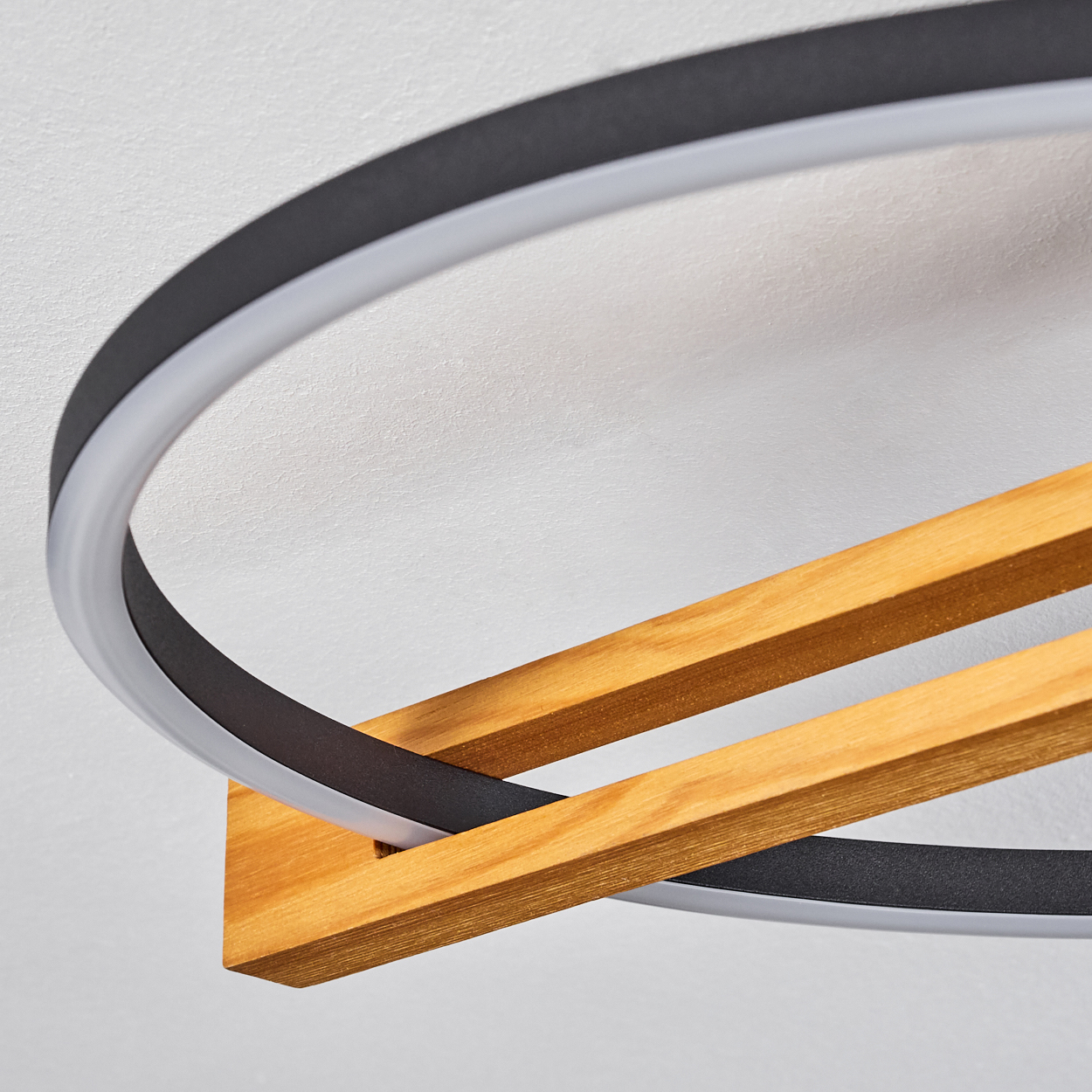 Eine moderne Deckenlampe. Sie hat ein kreisförmiges schwarz-weißes Licht und Holzbalken, die es kreuzen. Der Hintergrund ist weiß.