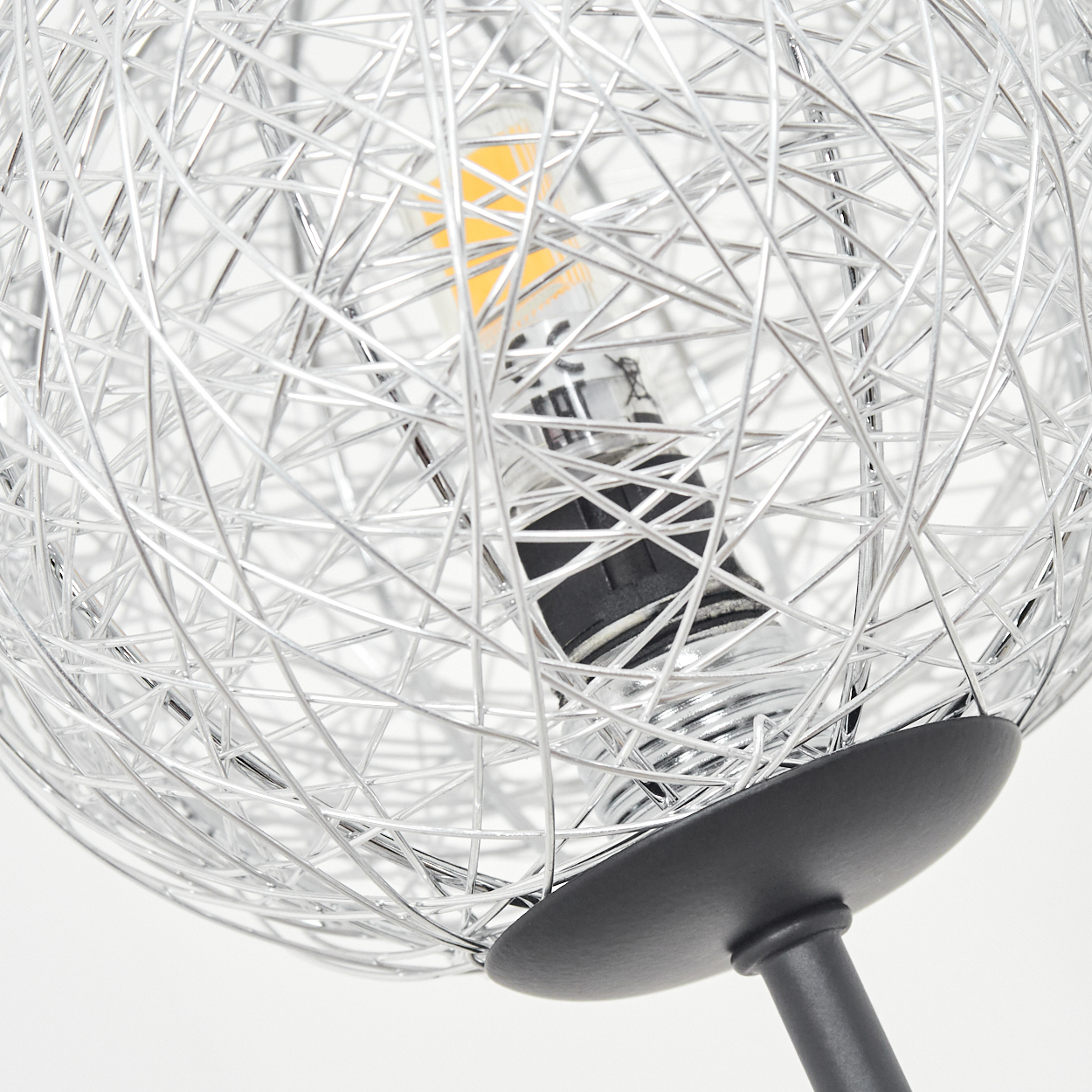 Nahaufnahme einer silbernen Drahtkugellampe. Eine Glühbirne ist innen. Die Lampe hat einen schwarzen Sockel und Stiel. Weißer Hintergrund.