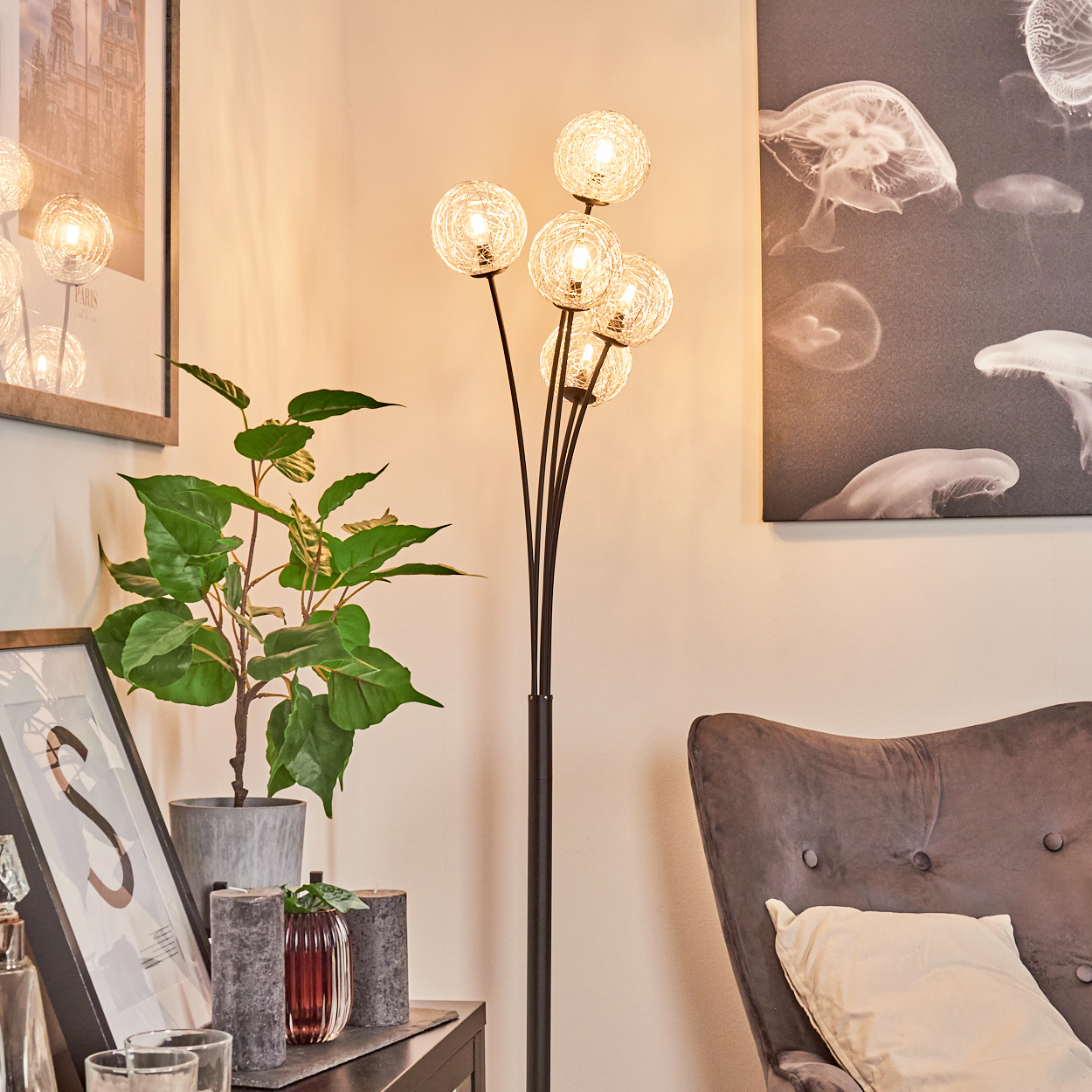 Eine Stehlampe mit Kugelleuchten. Eine Pflanze, ein gerahmtes Bild, ein dunkler Stuhl und ein Quallenkunstwerk sind vorhanden.