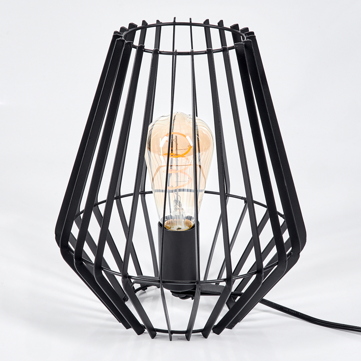 Eine schwarze Metallkäfiglampe mit einer großen bernsteinfarbenen Glühbirne auf weißem Hintergrund. Die Lampe hat ein geometrisches Design.