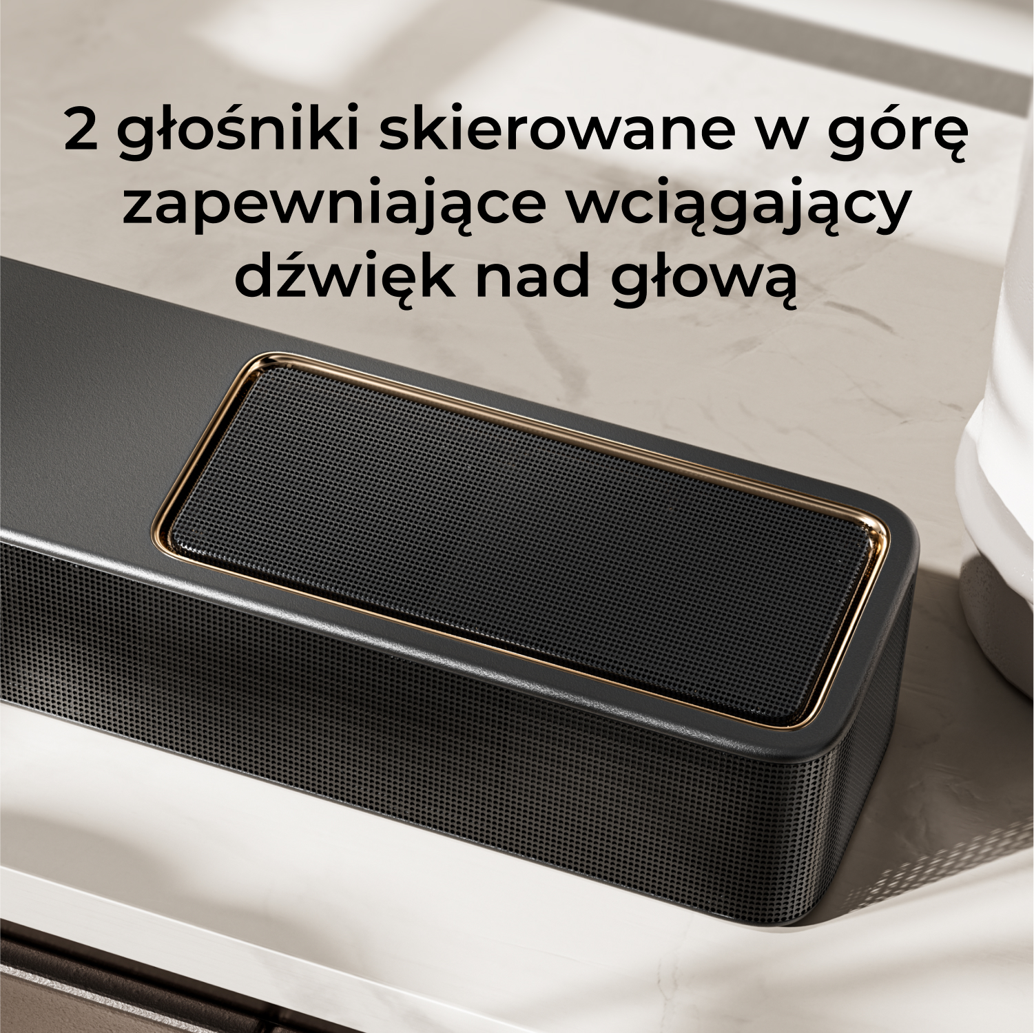 Czarny soundbar ze złotym wykończeniem, skierowany w górę. Leży na białej powierzchni.