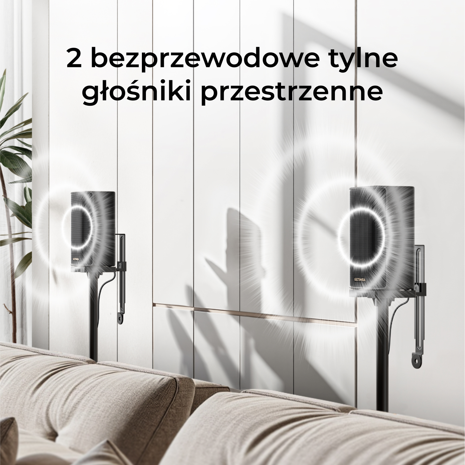 Wyświetlane są dwa czarne, bezprzewodowe głośniki tylne, umieszczone na stojakach, w pobliżu beżowej sofy, z białą ścianą w tle.
