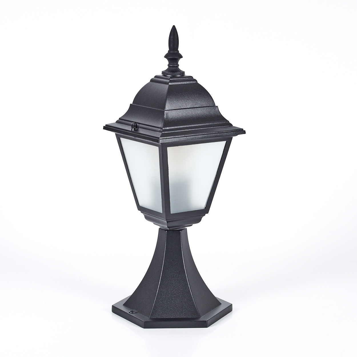 Eine schwarze Außenlampe mit spitzer Spitze. Sie hat einen Glasteil und steht auf einem Sockel vor weißem Hintergrund.
