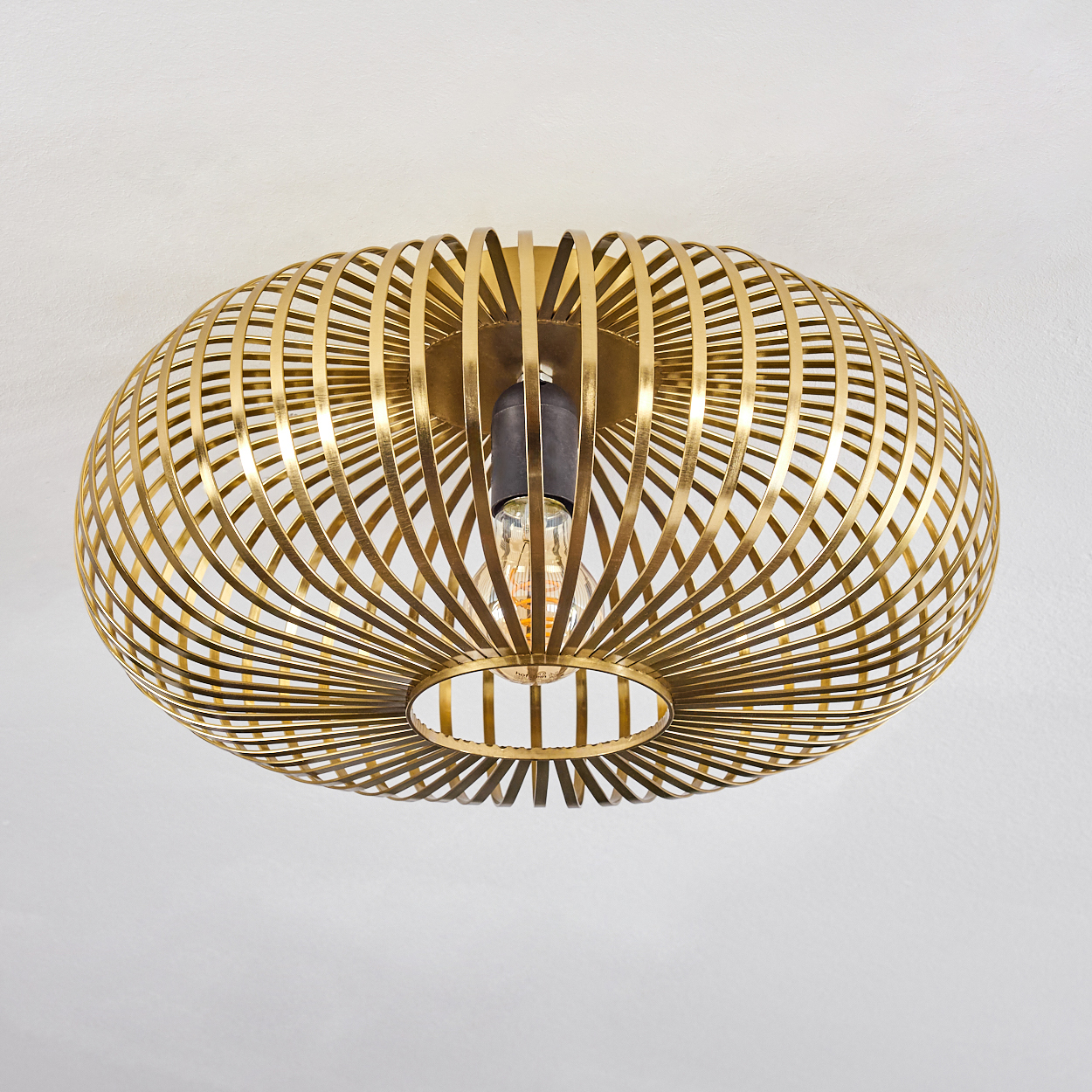Eine goldene, kugelförmige Deckenleuchte mit Gitterwerk-Design. Die Glühbirne ist im Inneren sichtbar. Sie befindet sich an einer weißen Decke.