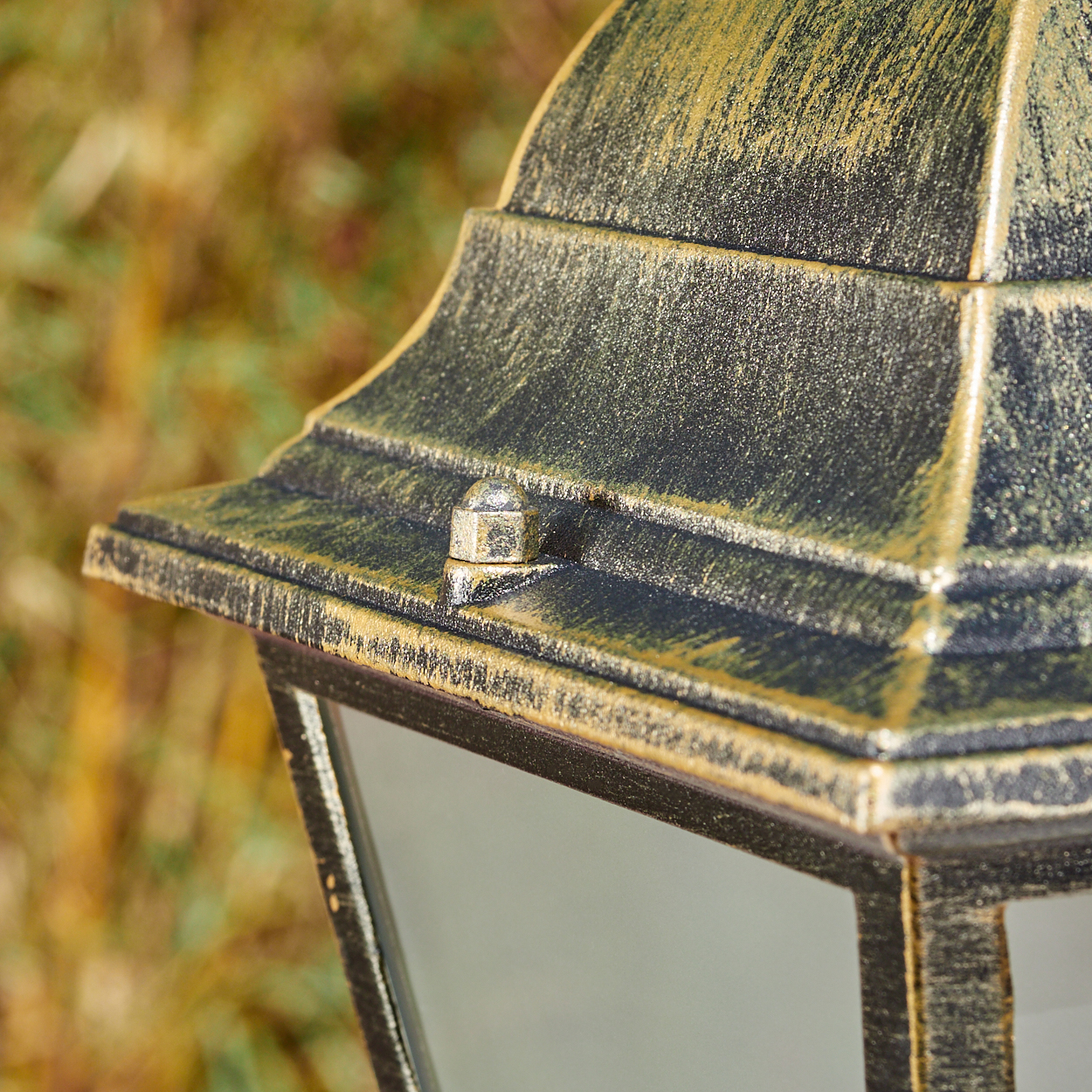 Nahaufnahme einer verzierten schwarzen und goldenen Außenlampe. Der Hintergrund ist verschwommenes Grün. Die Lampe ist detailliert mit Metallic-Finish.