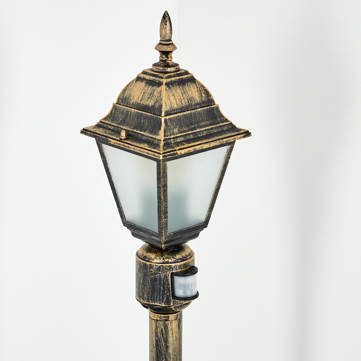 Eine bronzefarbene Außenlaterne mit Bewegungssensor. Die Lampe hat eine dekorative Spitze und Milchglasscheiben.