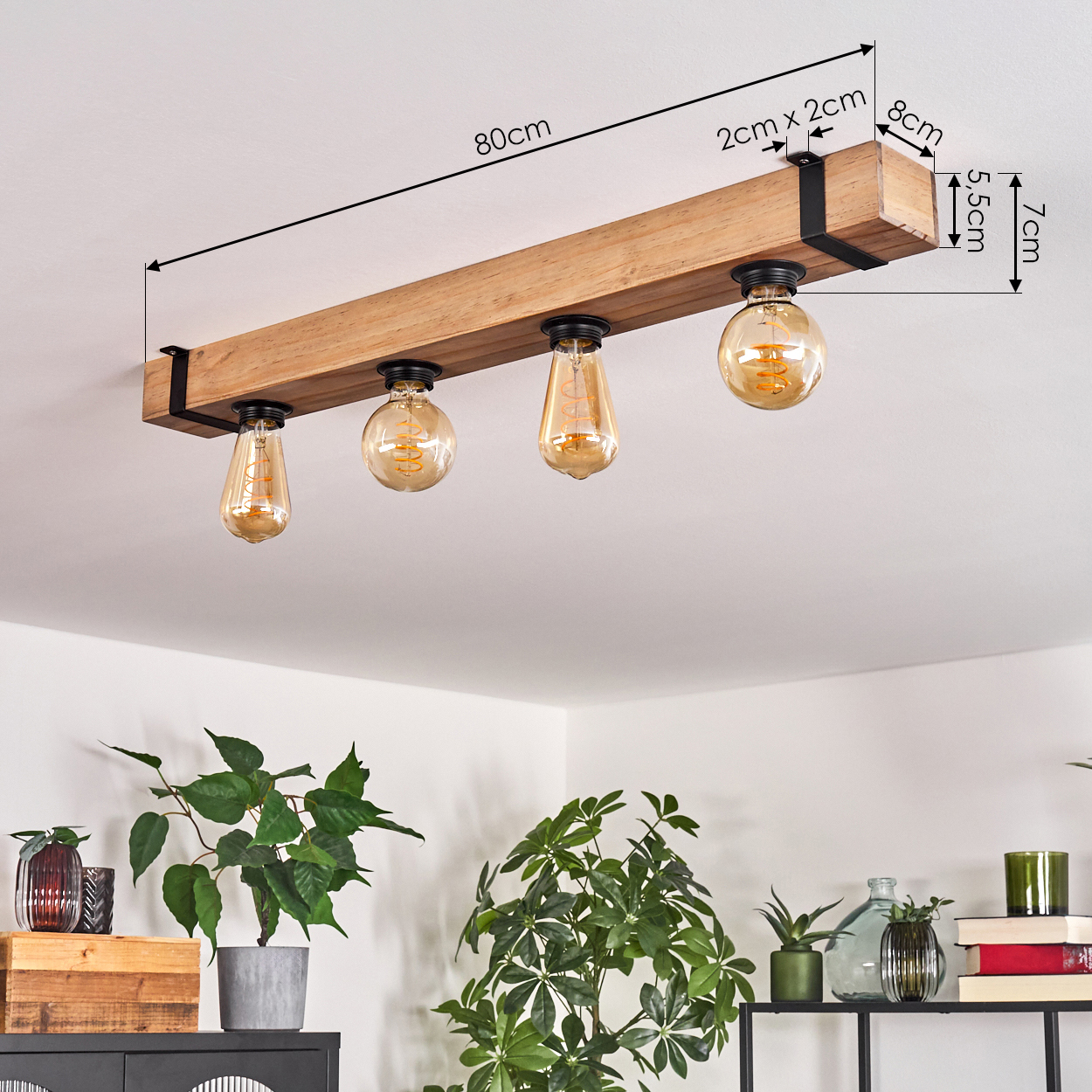 Holzbalken-Deckenleuchte mit vier leuchtenden Glühbirnen. Darunter Pflanzen und Deko auf einem schwarzen Schrank und Regal.