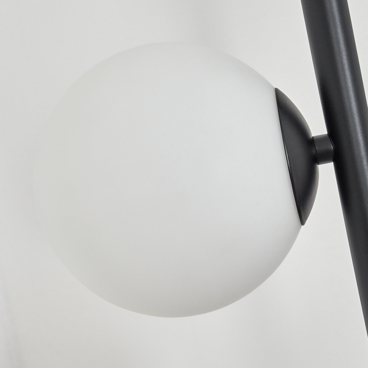 Nahaufnahme einer modernen Lampe. Sie hat einen weißen Kugelschirm und eine schwarze Metallstütze. Der Hintergrund ist schlicht weiß.