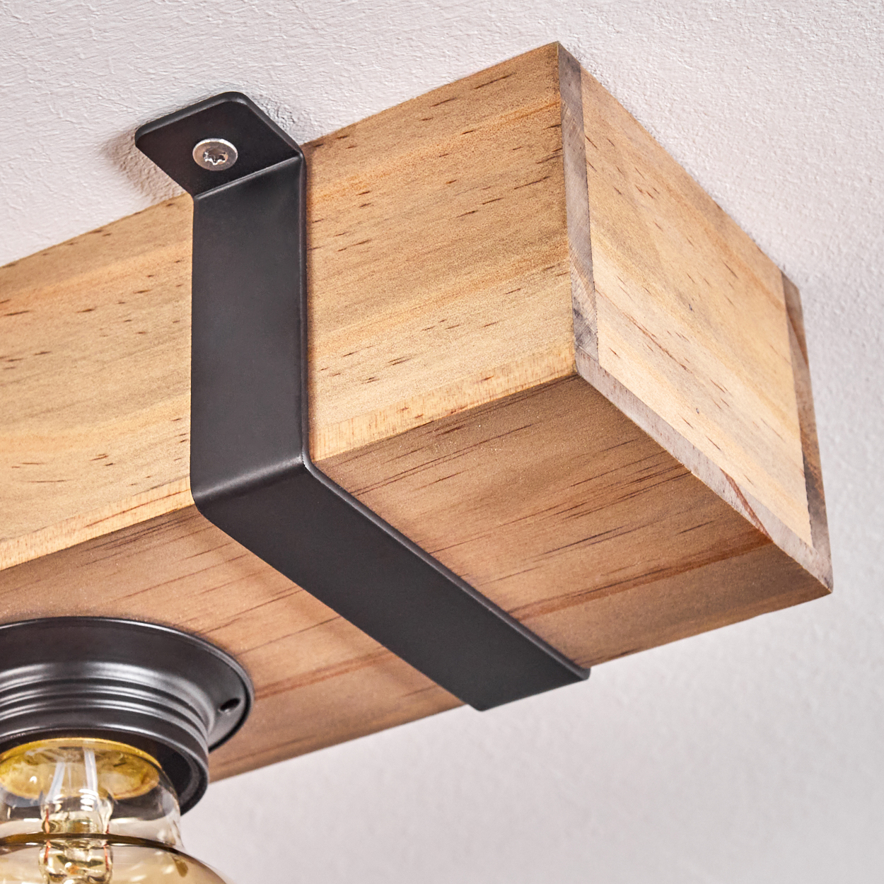 Holzbalken, befestigt mit schwarzen Metallwinkeln an einer weißen Decke. Unter dem Balken ist eine Leuchte mit gelber Glühbirne zu sehen.