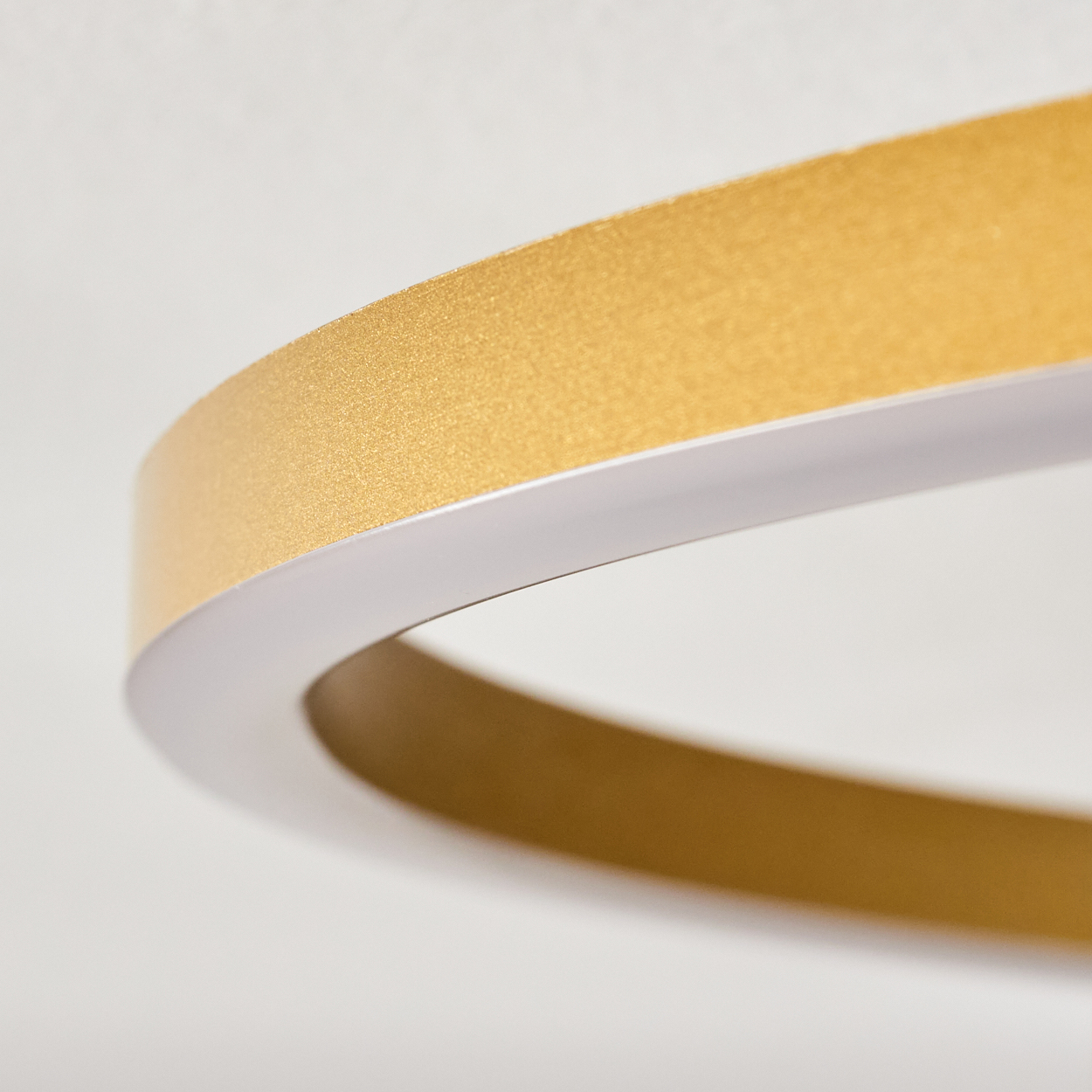 Nahaufnahme einer goldenen, kreisförmigen Leuchte. Der Ring ist goldfarben mit weißem Rand, vor weißem Hintergrund.