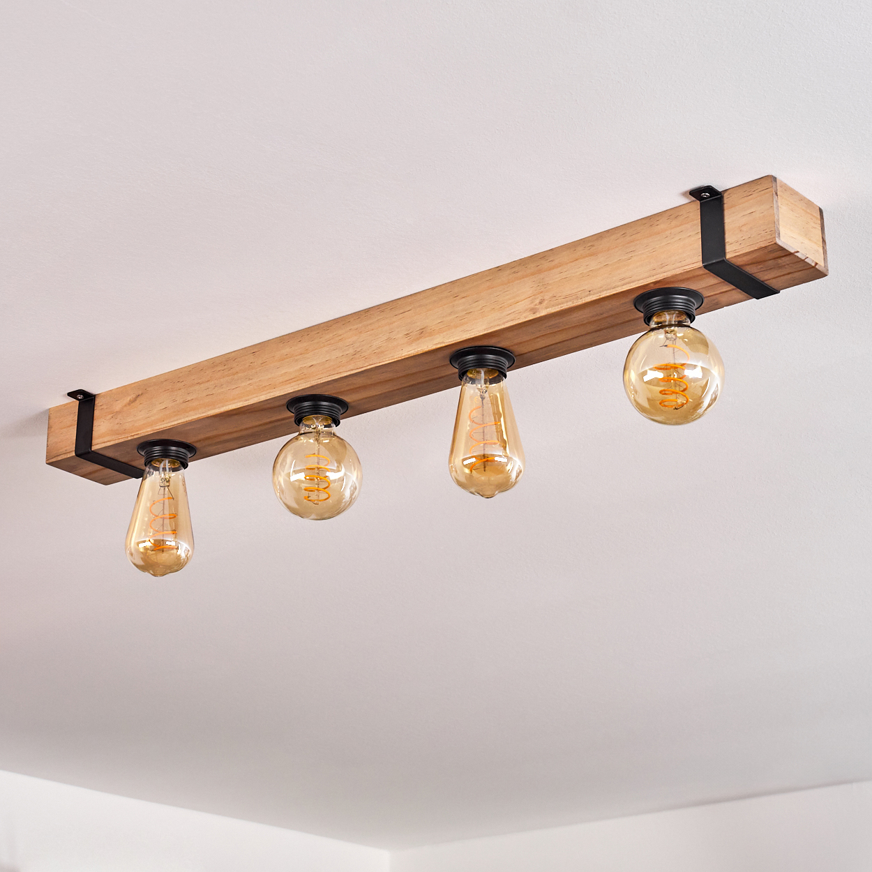 Eine Deckenleuchte aus Holzbalken mit vier bernsteinfarbenen Glühbirnen. Das Licht ist an einer weißen Decke montiert.