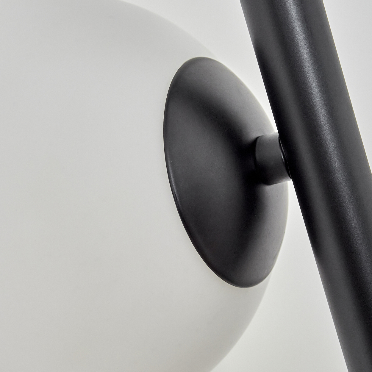 Nahaufnahme einer modernen Lampe. Eine weiße Kugel ist an einem schwarzen Metallarm befestigt. Der Hintergrund ist weiß.