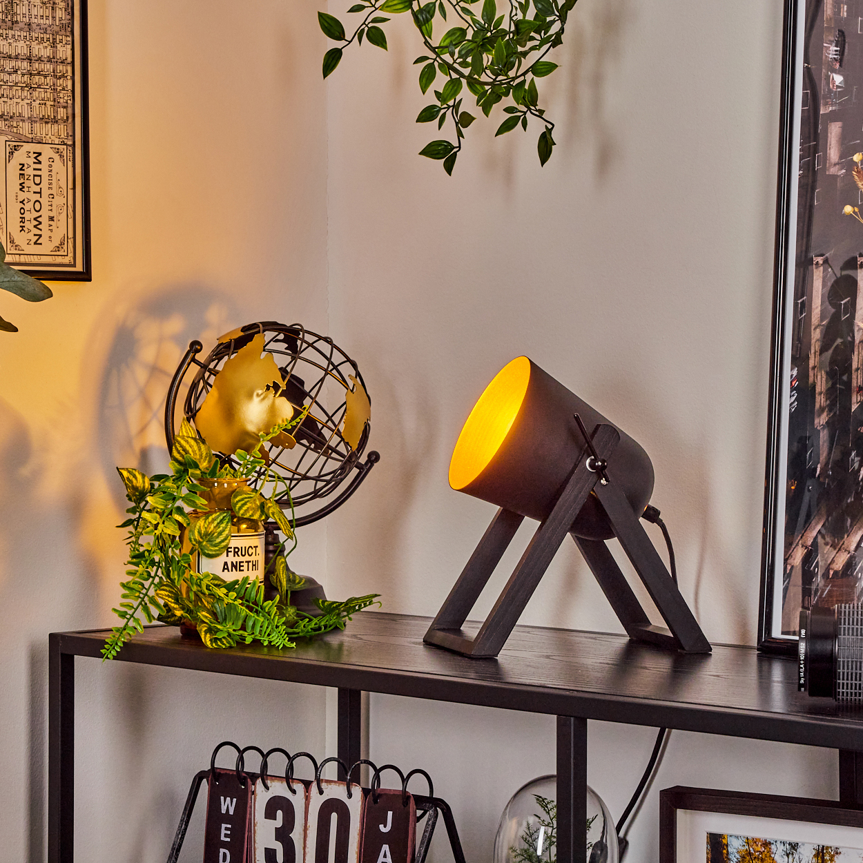 Eine Schreibtischlampe mit gelbem Licht, ein Globus, eine Pflanze, ein Kalender und andere dekorative Gegenstände auf einem schwarzen Regal.