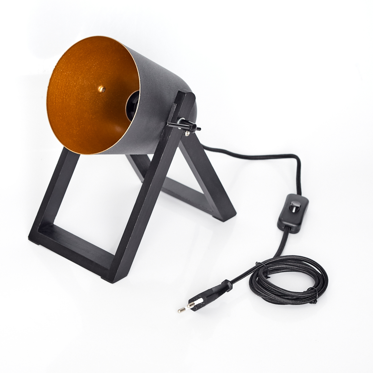 Schwarze und goldene Schreibtischlampe auf weißer Oberfläche. Sie hat einen zylindrischen Schirm und einen Holzfuß. Ein Netzkabel und ein Schalter sind sichtbar.