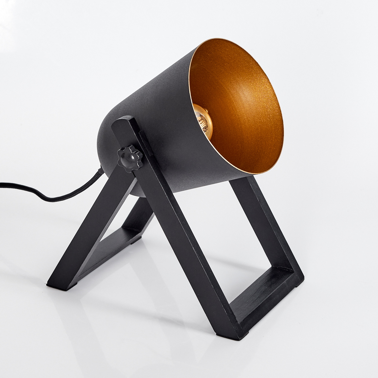 Eine schwarze Schreibtischlampe mit goldfarbenem Innenraum, getragen von einem schwarzen Rahmen. Die Lampe steht auf einer weißen Oberfläche.