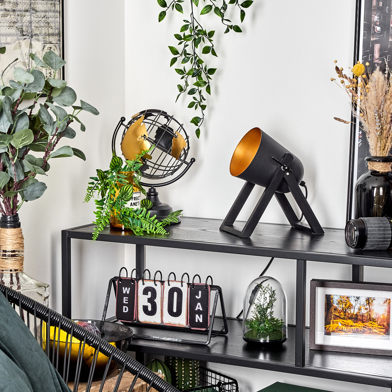Ein schwarzes Regal mit dekorativen Gegenständen: Lampe, Globus, Kalender, Pflanzen und gerahmtes Bild. Neutraler Hintergrund.