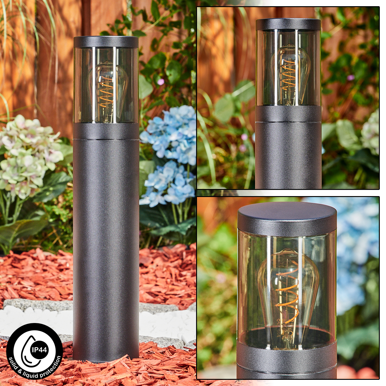 Eine schwarze Außenlampe mit Glaskopf und dekorativer Glühbirne. Sie steht auf roter Mulch. Im Hintergrund Pflanzen und ein Holzzaun.