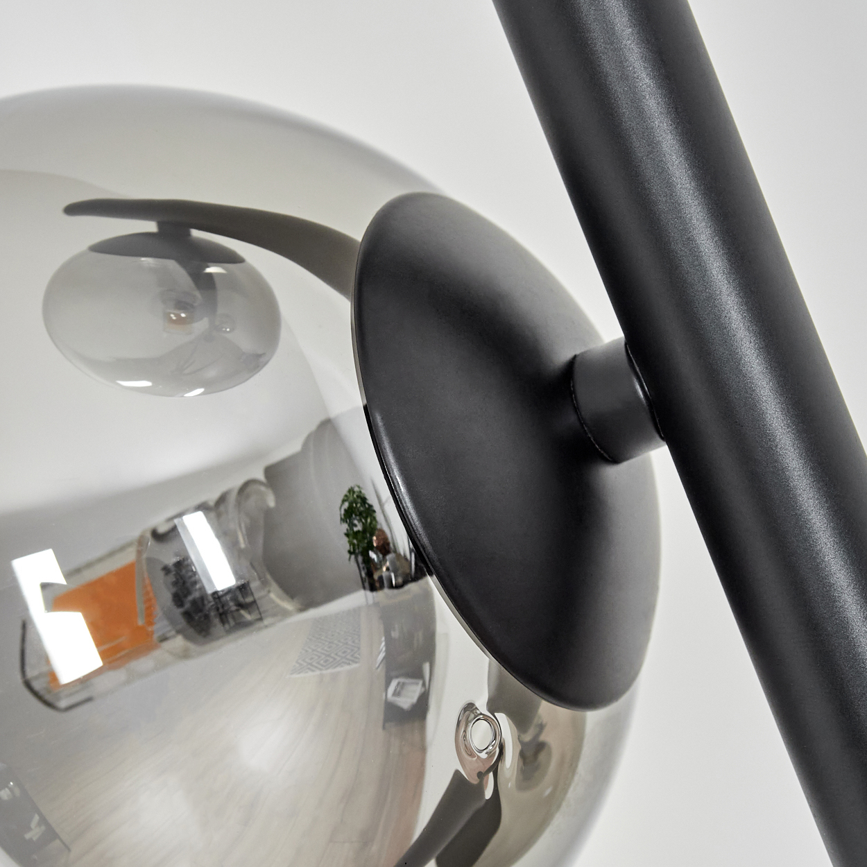 Nahaufnahme einer modernen Lampe. Sie hat eine graue Glaskugel, schwarze Metalldetails und einen schwarzen Arm. Der Hintergrund ist weiß.