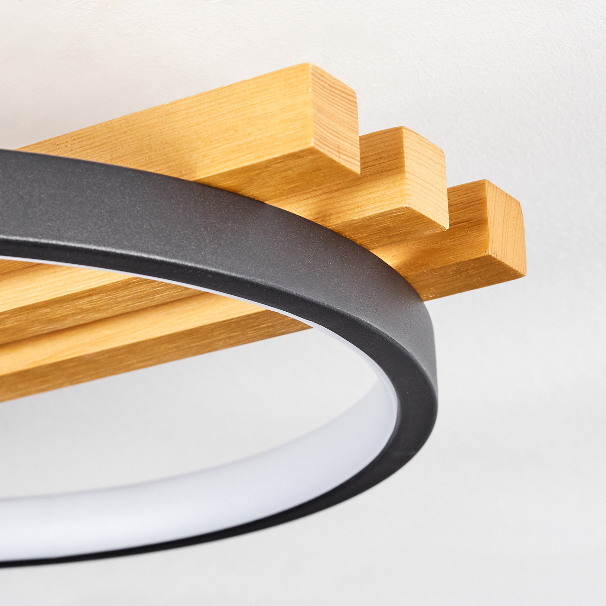 Nahaufnahme einer modernen Deckenleuchte. Sie hat einen schwarzen Ring mit einem weißen Innenring und Holzbohlen darüber.