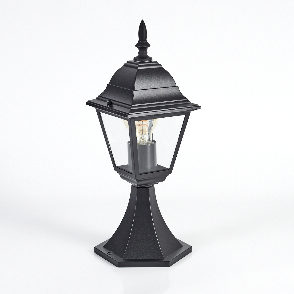 Eine schwarze Außenlampe auf weißem Hintergrund. Die Lampe hat ein klares Glasgehäuse mit einer leuchtenden Glühbirne. Sie steht auf einem Sockel.