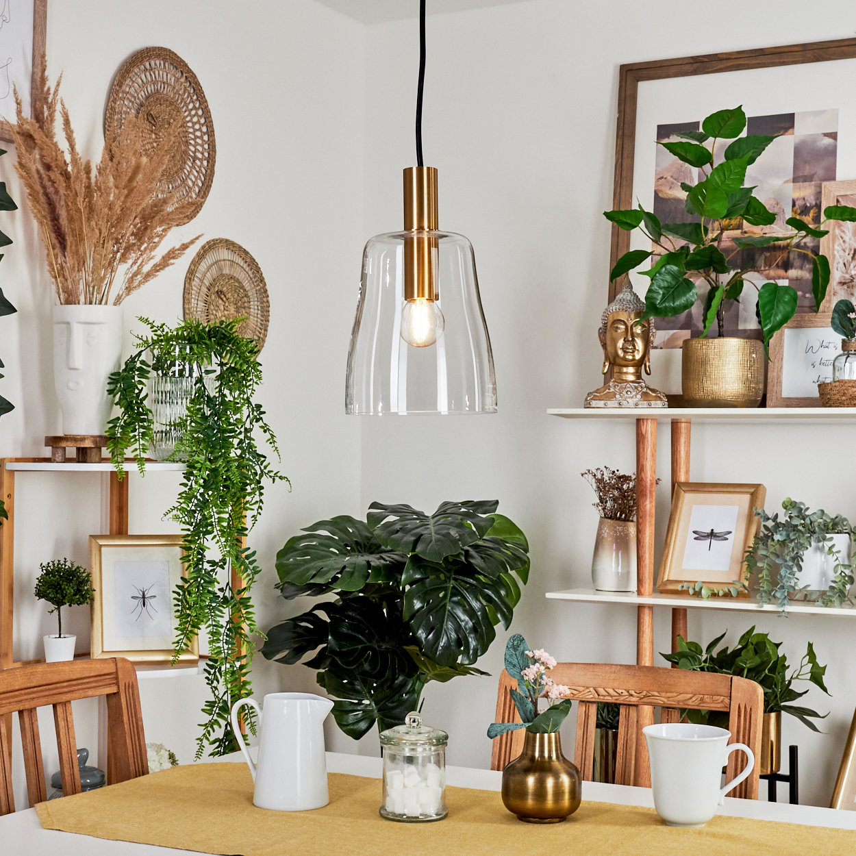 Ein Esszimmer mit einem Tisch für zwei Personen. Pflanzen und Dekorationen schmücken die Wände. Über dem Tisch hängt eine klare Glas-Pendelleuchte.
