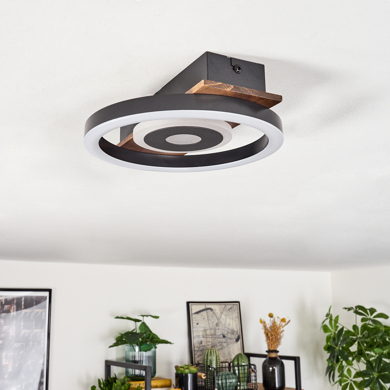 Moderne Deckenleuchte mit schwarzem und Holzdesign. Pflanzen und Dekorationen sind im Hintergrund sichtbar.
